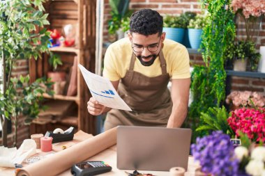 Young arab man florist using laptop reading document at florist