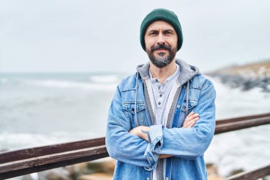 Kel genç adam sahilde kollarını kavuşturmuş el kol hareketi yapıyor.