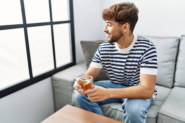 Genç Arap adam evde çay içerek kendinden emin gülümsüyor.