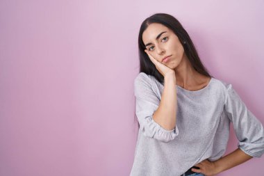 Young brunette woman standing over pink background thinking looking tired and bored with depression problems with crossed arms. 