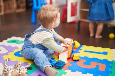 Adorable toddler playing with car toy sitting on floor at kindergarten