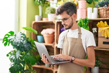 Young hispanic man florist using laptop with relaxed expression at flower shop