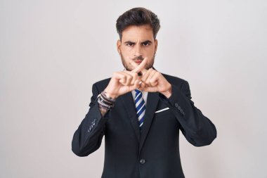 Young hispanic man with tattoos wearing business suit and tie rejection expression crossing fingers doing negative sign 
