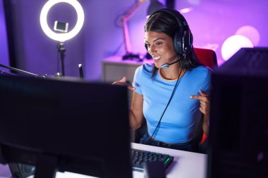 Brunette young woman playing video games looking confident with smile on face, pointing oneself with fingers proud and happy. 