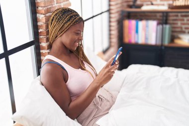 Afrika kökenli Amerikalı bir kadın yatak odasında akıllı telefon kullanıyor.