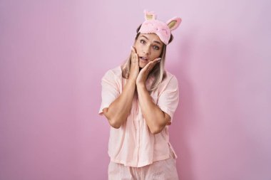 Blonde caucasian woman wearing sleep mask and pajama tired hands covering face, depression and sadness, upset and irritated for problem 