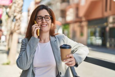 Genç iş kadını akıllı telefondan konuşuyor. Sokakta kahve içiyor.