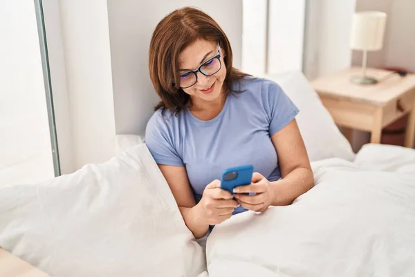 Medelålders Kvinna Med Smartphone Sittande Sängen Sovrummet — Stockfoto