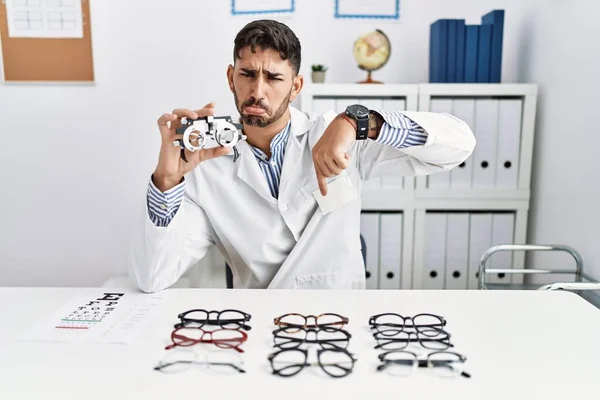 Young Optician Man Holding Optometry Glasses Pointing Looking Sad Upset — 图库照片