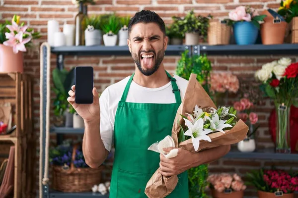 Латиноамериканец Работающий Цветочном Магазине Показывает Экран Смартфона Торчащий Языком Довольный — стоковое фото