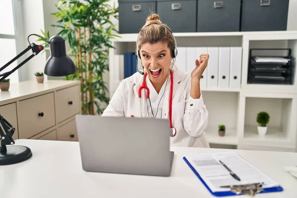 Young doctor woman wearing doctor uniform working using computer laptop celebrating victory with happy smile and winner expression with raised hands