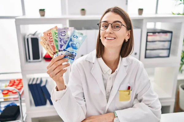 Young Caucasian Doctor Woman Holding Canadian Dollars Banknotes Looking Positive — Stock Photo, Image