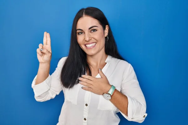 Ung Spansktalende Kvinde Stående Blå Baggrund Smilende Sværger Med Hånd - Stock-foto