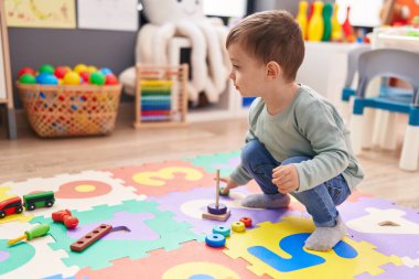 Adorable hispanic boy playing with hoops toys standing at kindergarten