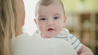 Sevimli beyaz bebek anne kollarına güvenerek gülümsüyor.