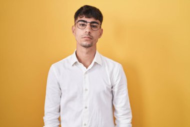 Young hispanic man standing over yellow background relaxed with serious expression on face. simple and natural looking at the camera. 