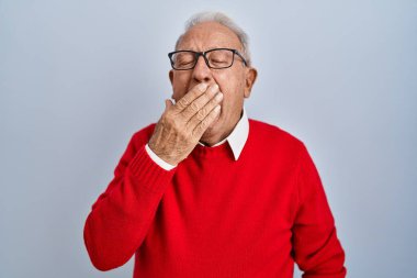 Senior man with grey hair standing over isolated background bored yawning tired covering mouth with hand. restless and sleepiness. 