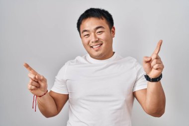 Young chinese man standing over white background smiling confident pointing with fingers to different directions. copy space for advertisement 