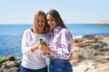 Two women mother and daughter using smartphone at seaside