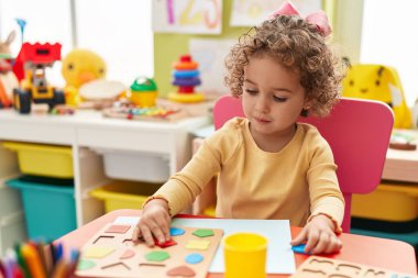 Adorable hispanic toddler playing with maths puzzle game sitting on table at kindergarten