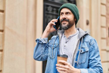 Genç kel adam akıllı telefondan konuşuyor. Sokakta kahve içiyor.
