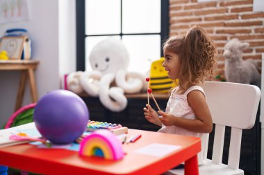 Adorable hispanic girl playing xylophone sitting on table at kindergarten