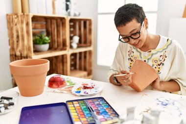 Sanat atölyesinde kilden seramik boyarken gülümseyen genç İspanyol kadın.