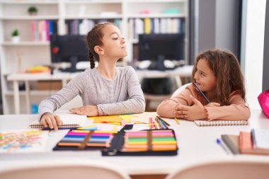 Two kids students sitting on table drawing on notebook paper at classroom