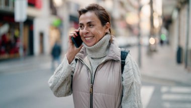 Orta yaşlı İspanyol kadın gülümsüyor. Akıllı telefondan konuşuyor.