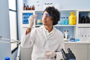 Laboratuvarda elinde cımbızla bilim adamı üniforması giyen genç bir İspanyol.