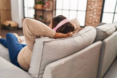 Orta yaşlı İspanyol kadın evdeki kanepede oturmuş müzik dinliyor.