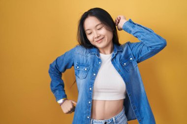 Young asian woman standing over yellow background stretching back, tired and relaxed, sleepy and yawning for early morning 