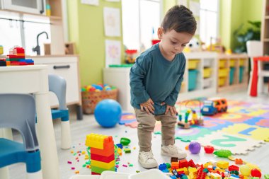 Adorable hispanic boy playing with construction blocks standing at kindergarten