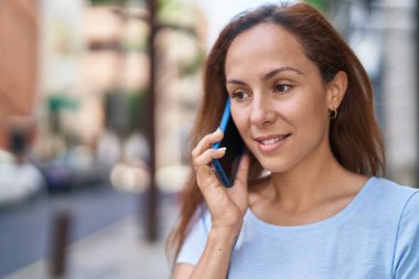 Gülümseyen genç bir kadın caddedeki akıllı telefondan konuşuyor.