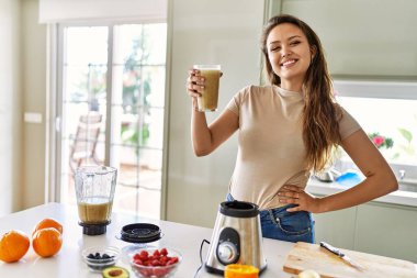 Genç ve güzel İspanyol kadın gülümsüyor. Mutfakta elinde bir bardak sebze suyu tutuyor.