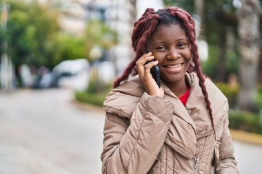 Afro-Amerikalı kadın gülümsüyor. Akıllı telefondan konuşuyor.