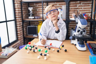 Sınıfta şüpheli bir ifadeyle not defterine yazan sevimli çocuk.