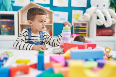 Adorable caucasian boy sitting on table playing with toys at kindergarten