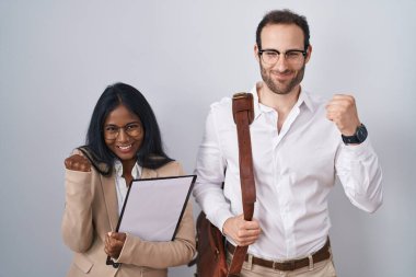 Interracial business couple wearing glasses very happy and excited doing winner gesture with arms raised, smiling and screaming for success. celebration concept. 
