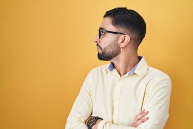 Hispanic young man wearing business clothes and glasses looking to the side with arms crossed convinced and confident 