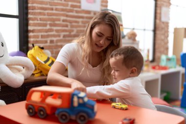 Öğretmen ve yeni yürümeye başlayan çocuk, anaokulundaki masada oturan oyuncaklarla oynuyor.