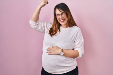 Pregnant woman standing over pink background angry and mad raising fist frustrated and furious while shouting with anger. rage and aggressive concept. 