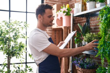 Çiçekçide çiçek ve pano tutan İspanyol bir adam.