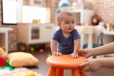 Sevimli Çinli çocuk gülümsüyor. Anaokulunda duran tabureye yaslanıyor.