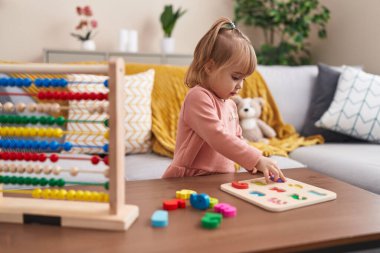 Adorable blonde girl playing maths puzzle game standing at home