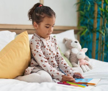 Yatak odasına oturmuş defterine resim çizen sevimli İspanyol kız.