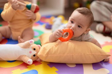 Two toddlers sucking toys sitting on floor at kindergarten clipart