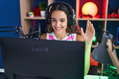 Young hispanic woman playing video games looking positive and happy standing and smiling with a confident smile showing teeth 
