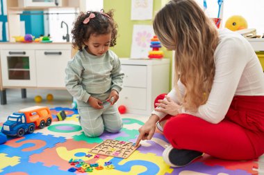 Teacher and toddler playing with maths puzzle game sitting on floor at kindergarten