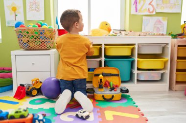 Beyaz tenli sevimli bir çocuk anaokulunda yerde oturmuş oyuncaklarla oynuyor.